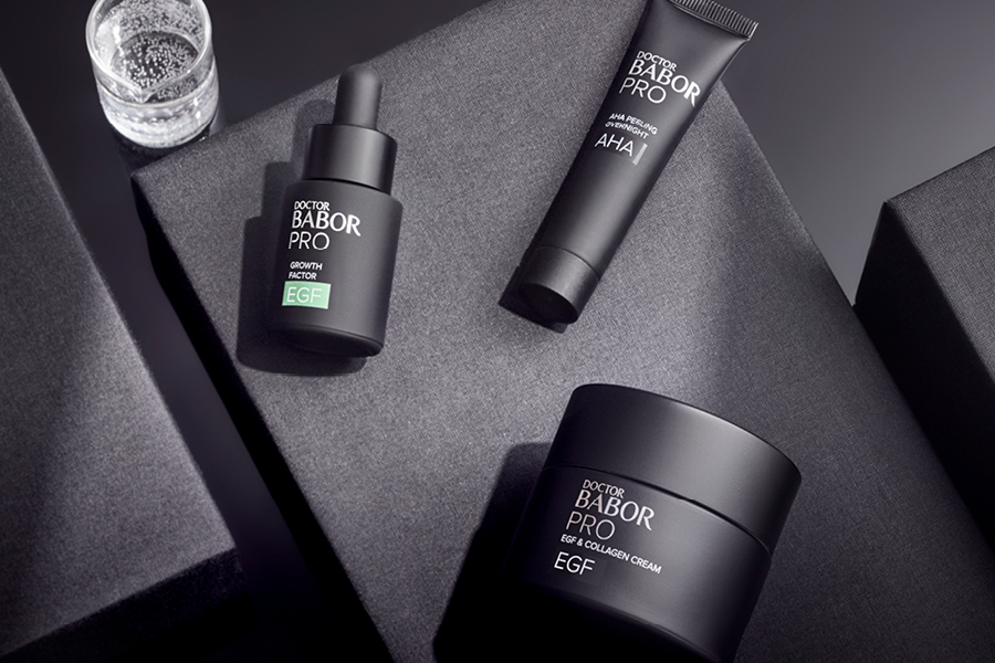 Drei elegante Doctor BABOR PRO Produkte – Serum, Peeling und Creme – stilvoll auf grauen Boxen arrangiert.